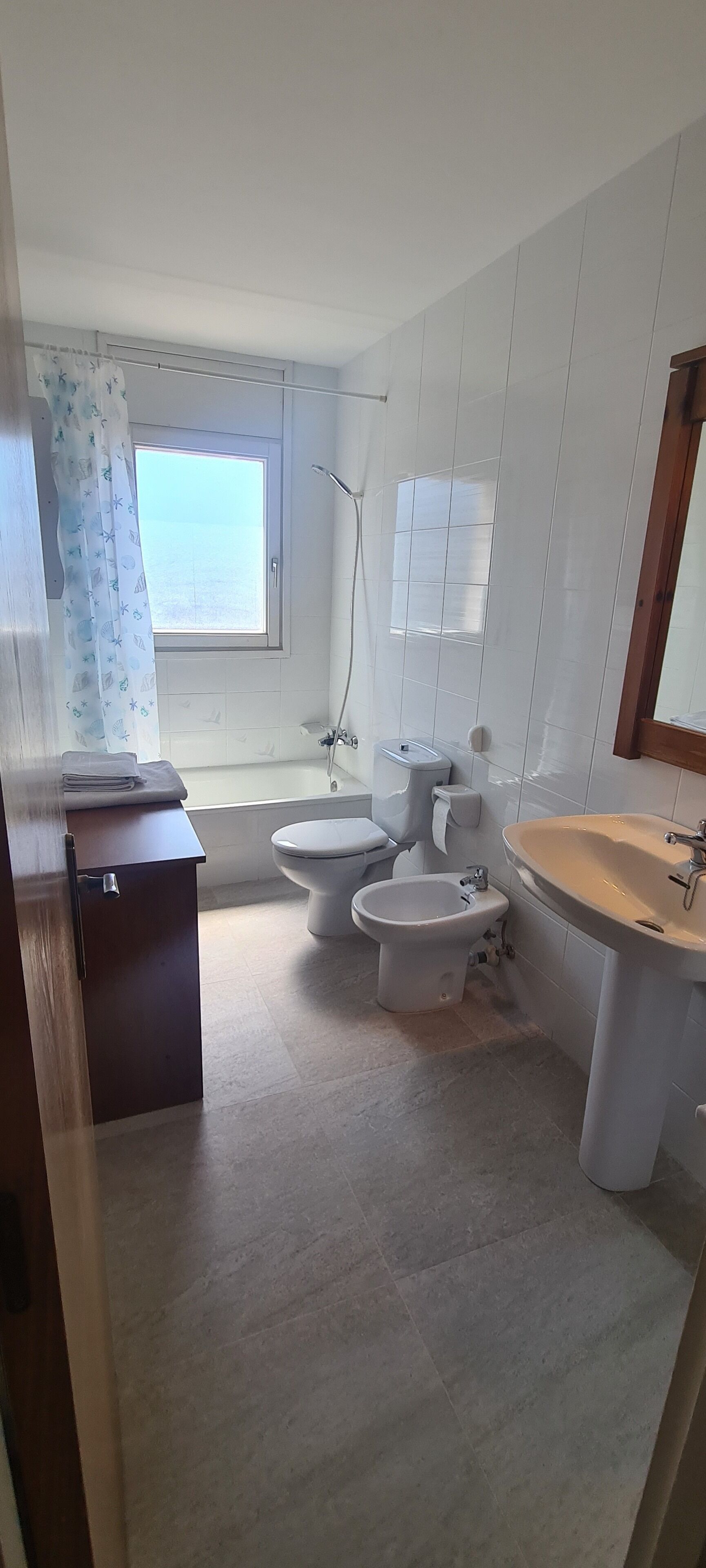 Een bad/douchecombinatie, een bidet, handdoeken, toiletpapier