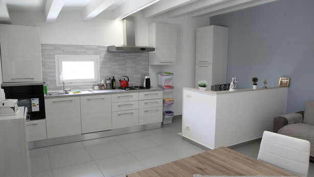 A modern kitchen with white cabinets, a wooden dining table, and a grey accent wall. - Happy House on two levels (Ragusa)