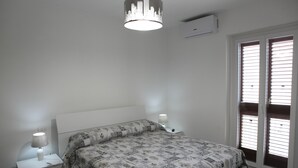 A bedroom with a bed, two bedside tables, a nightstand, a ceiling light fixture, and a window with blinds. - Happy House on two levels (Ragusa)