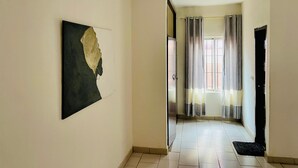 A hallway with a tiled floor, a door on the right, and a window with curtains. - Grand appartement de 3 chambres panoramique (Yaounde)