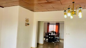 A spacious room with a wooden ceiling, a dining area with a table and chairs, and a chandelier. - Grand appartement de 3 chambres panoramique (Yaounde)