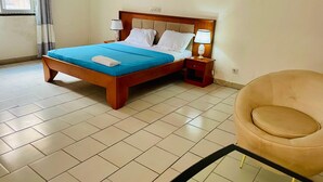 A neatly arranged hotel room with a bed, bedside lamps, a chair, and a tiled floor. - Grand appartement de 3 chambres panoramique (Yaounde)