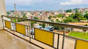A balcony with a view of a residential area, including houses and a parked car. - Grand appartement de 3 chambres panoramique (Yaounde)