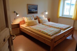 A double bed with striped bedding, two bedside lamps, a nightstand, a framed picture on the wall, and a window with curtains.