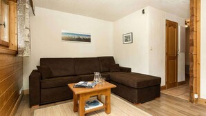 Een gezellige woonkamer met een bruine bank, een houten salontafel met boeken en glazen, en een klein vloerkleed.