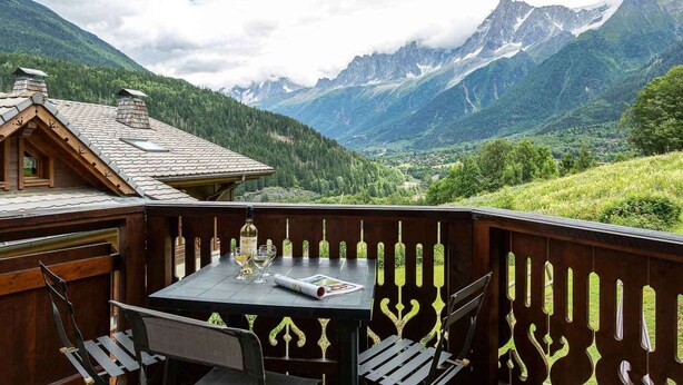 Een houten terras met een tafel en stoelen met uitzicht op een bergachtig landschap.