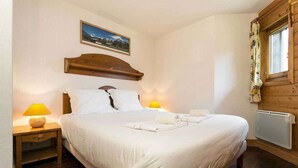 Een slaapkamer met een groot bed, twee bedlampen, een houten hoofdeinde, een raam met gordijnen en een ingelijste foto aan de muur.