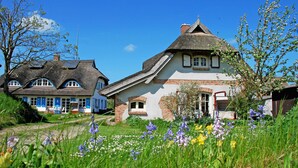 Ett traditionellt hus med ett halmtak, omgivet av en trädgård med olika sorters blommor.