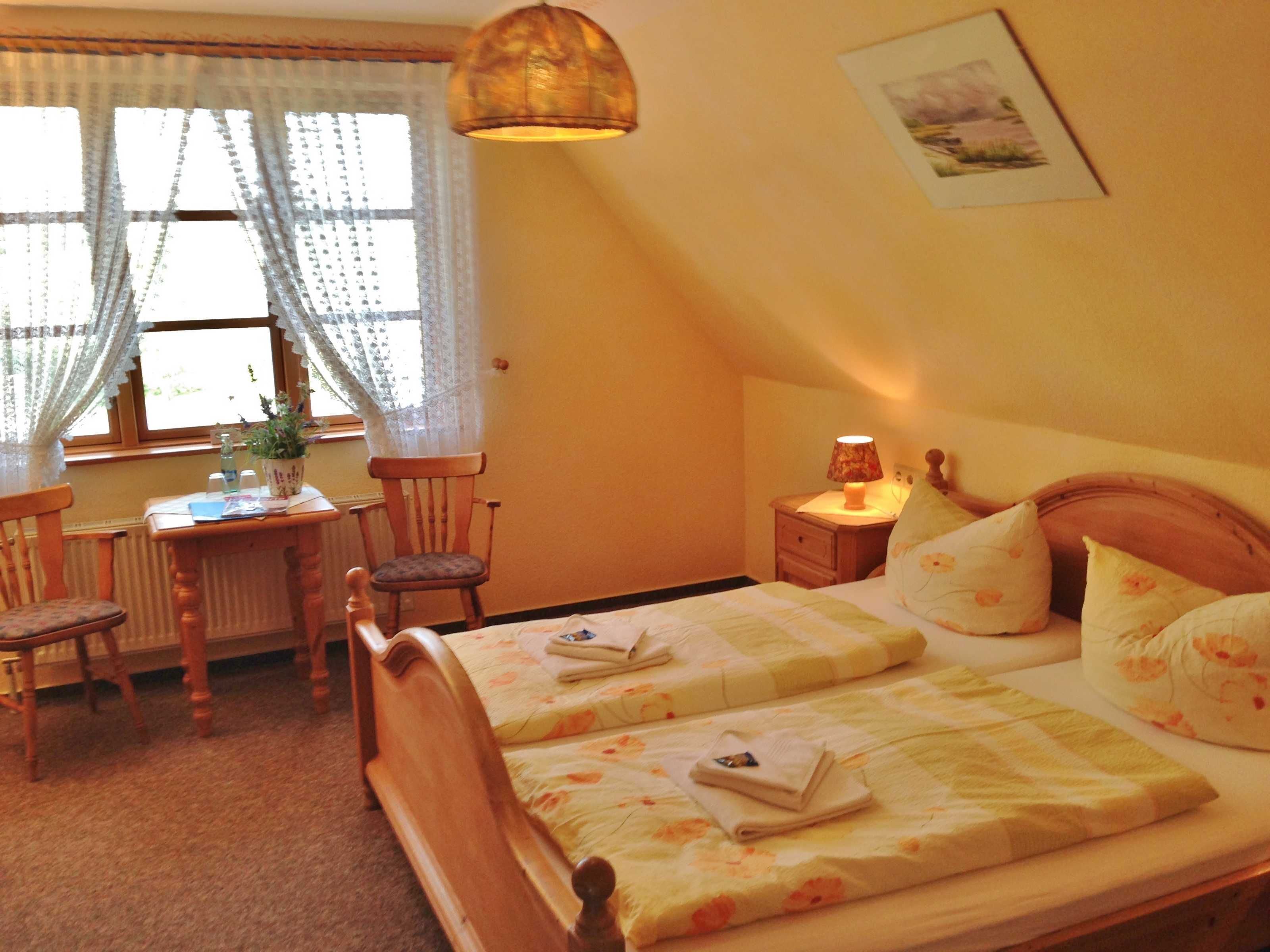 A bedroom with two beds, a desk, chairs, a lamp, and a window with curtains.