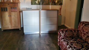 A room with a wooden cabinet, a white dresser, a patterned sofa, and a wall-mounted artwork. - 7 - "Up'n Hoff", Germany (Middelhagen)