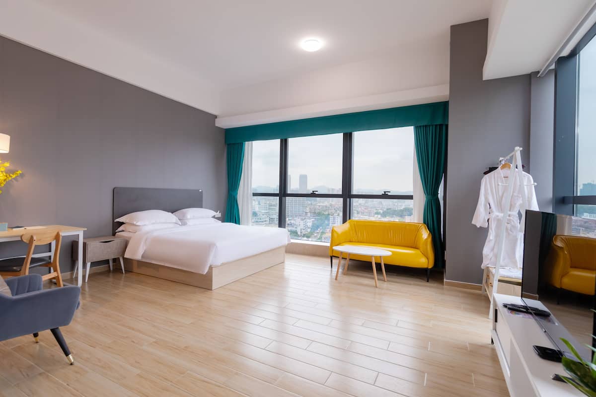 A modern hotel room with a large bed, a desk, a yellow sofa, and a TV.