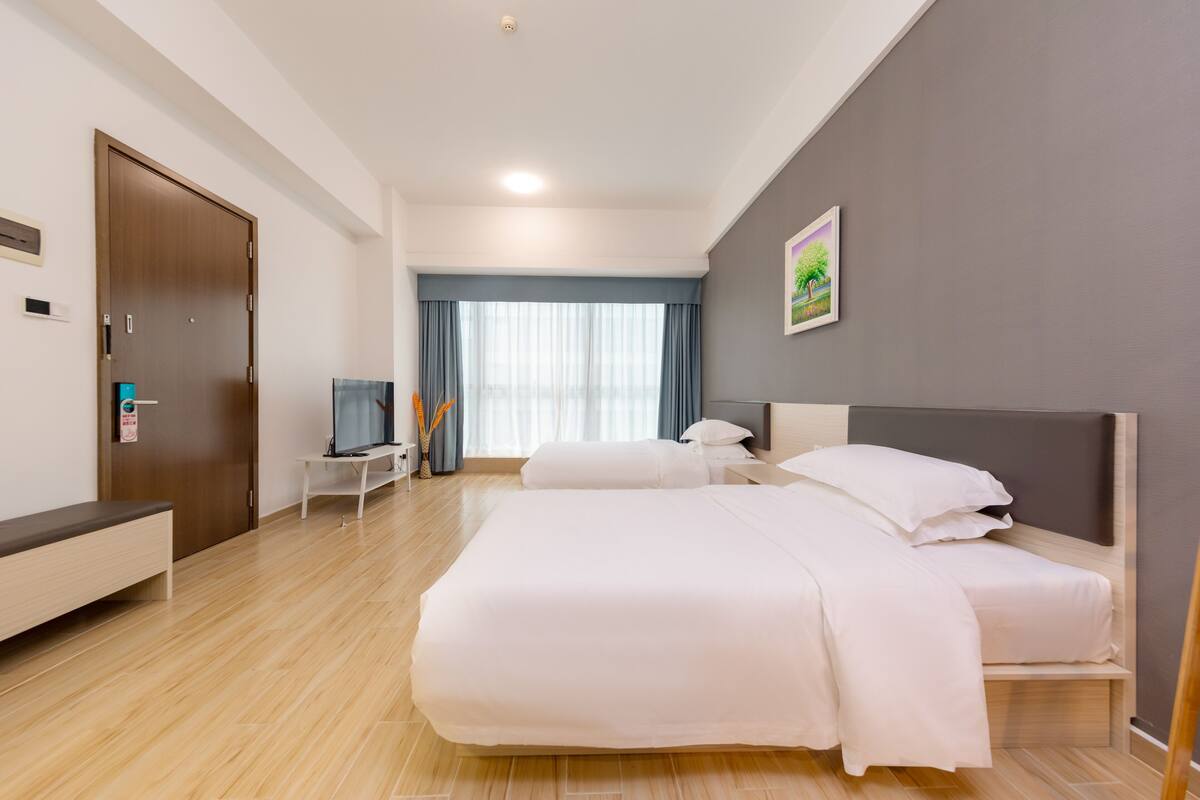 A hotel room with a large bed, a bedside table, a TV, and a window with curtains.