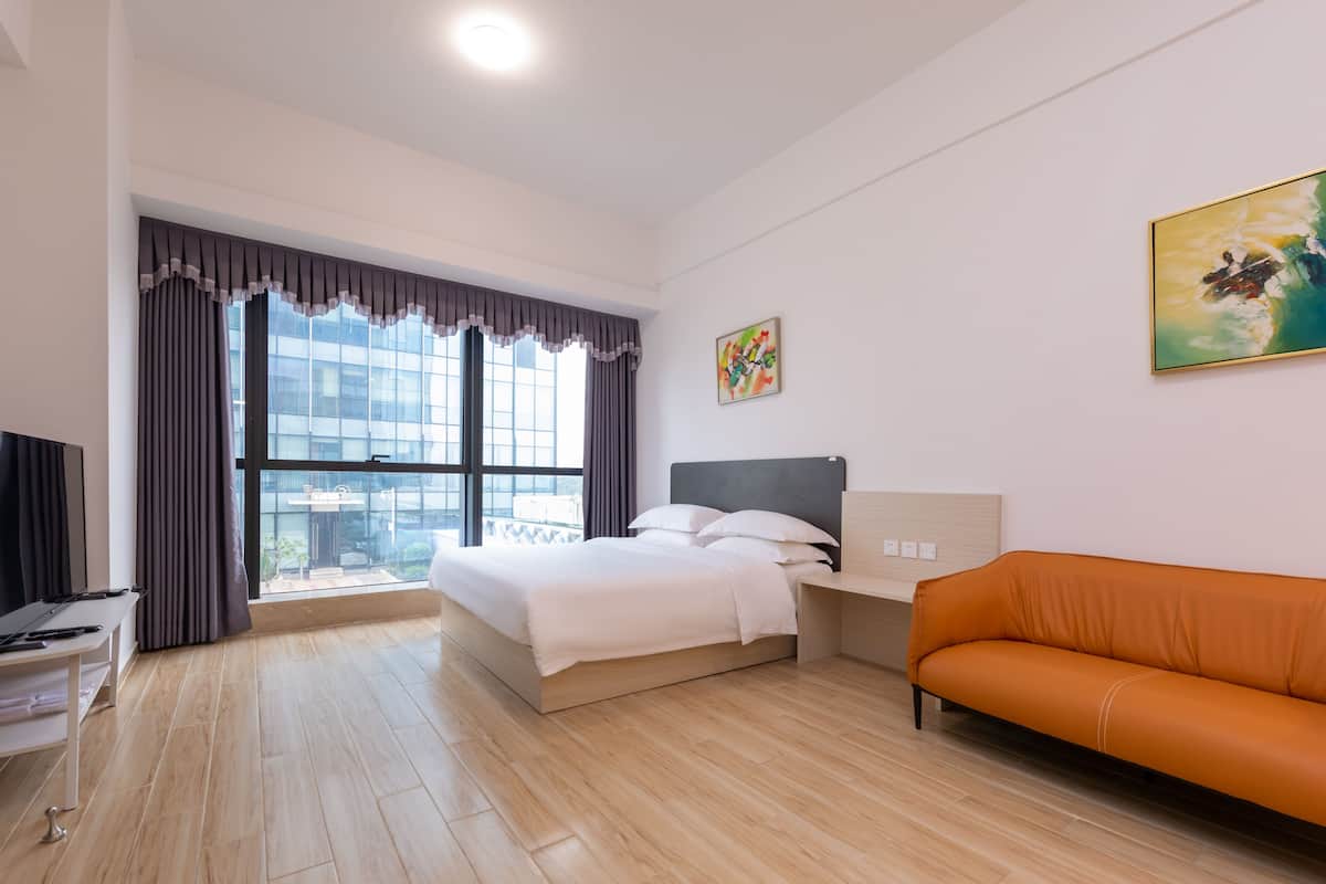 A modern hotel room with a large bed, an orange sofa, a desk, and a TV.