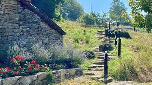 Un edificio de piedra con tejado de tejas rojas, rodeado de un muro de piedra y un jardín con flores rojas.