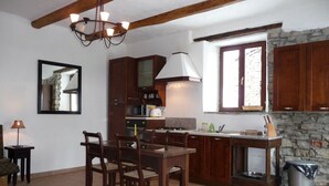 Una cocina con armarios de madera, una mesa de comedor con sillas, una araña y una pared de piedra.