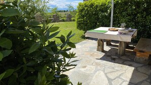 Un patio exterior con suelo de piedra, una mesa de madera con un posavasos verde y una copa de vino.