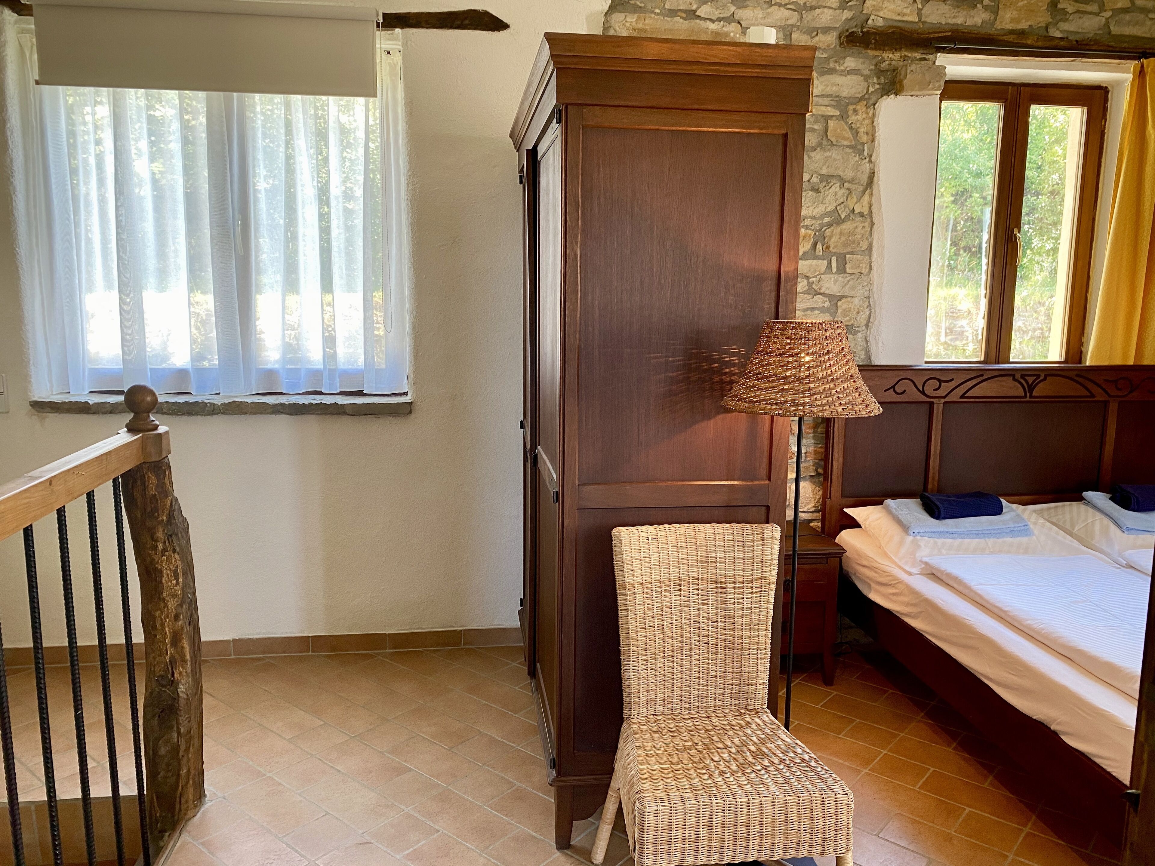 A bedroom with a bed, a wicker chair, a wardrobe, and a lamp.