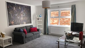 A modern living room with a grey sofa, a large abstract painting, a white radiator, and a TV on a glass table. - Fabulous Apartment in the City of Ripon, close to Cathedral with private parking (Ripon)