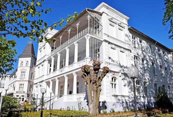 A large white building with a prominent balcony and columns, surrounded by greenery and street lamps.