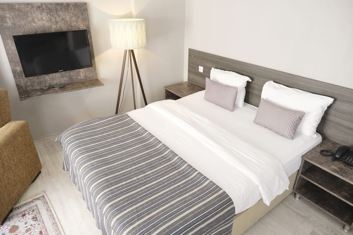 Une chambre d’hôtel avec un grand lit, un téléviseur à écran plat fixé au mur, une table de chevet avec une lampe et une petite table de nuit avec un téléphone.