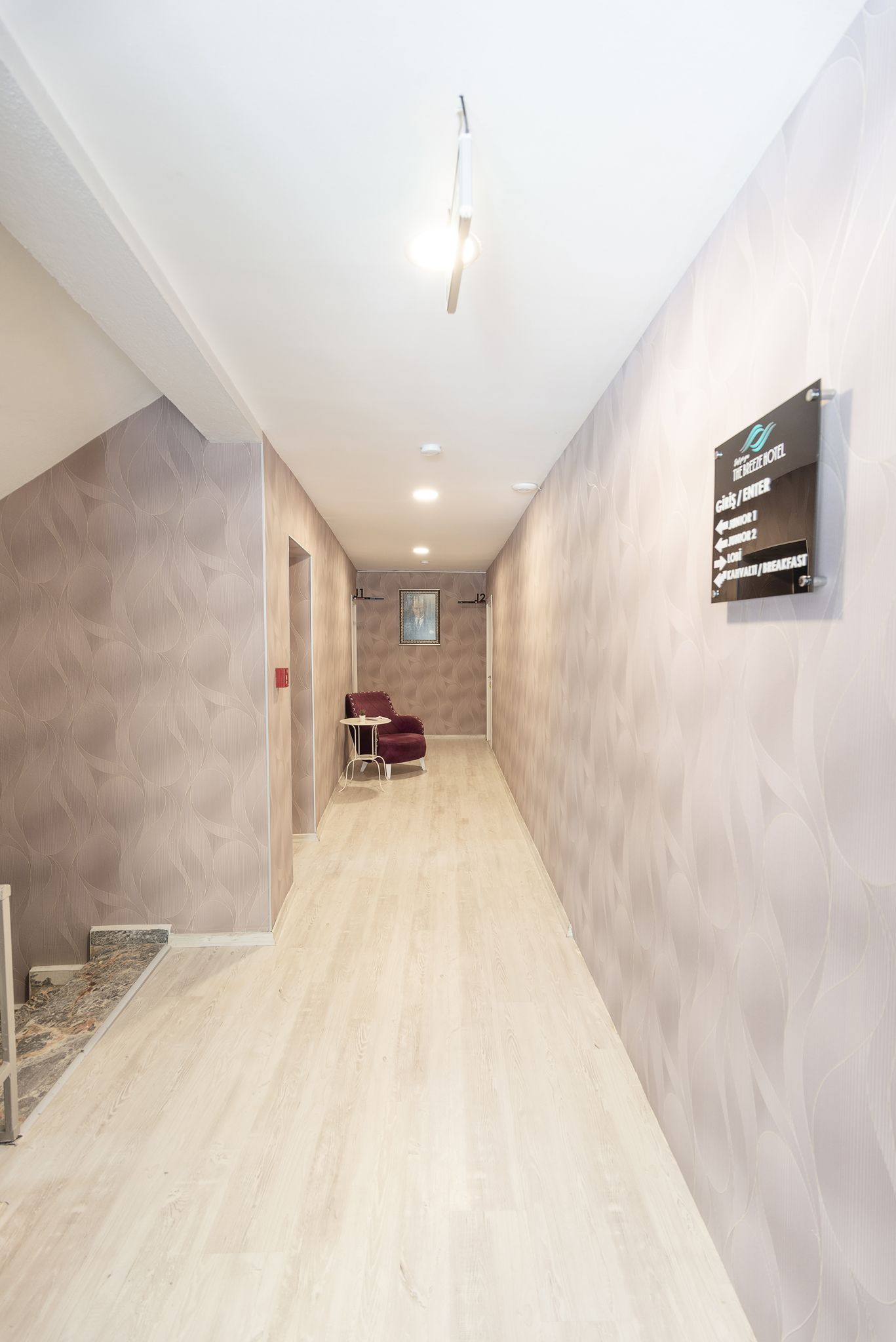 A hallway with a patterned wall, a red chair, and a sign indicating room numbers and services.
