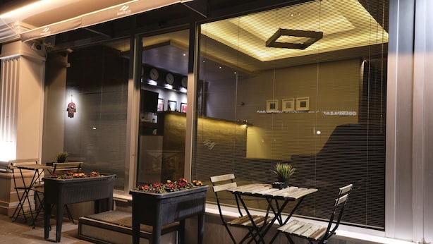 Un espace extérieur aménagé avec des tables et des chaises, un pot de fleurs et une fenêtre ornée d’une horloge et de tableaux encadrés.