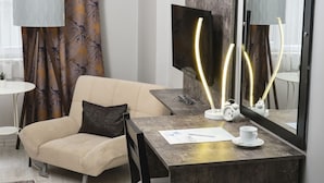 Une chambre d’hôtel moderne équipée d’un canapé, d’un bureau avec une lampe, d’une télévision à écran plat et d’un grand miroir.