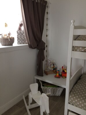 A child's bunk bed with a white frame, a small desk with toys, a basket, and a polka dot pillow. - Le Petit Monty (Saint-Malô-du-Bois)