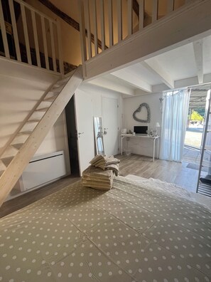 Una habitación con una escalera, una cama con edredón de lunares, un escritorio pequeño con una computadora y una ventana con cortinas.