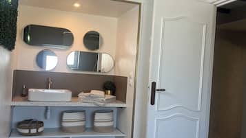 Une salle de bain avec un lavabo blanc, plusieurs miroirs et des étagères de rangement.