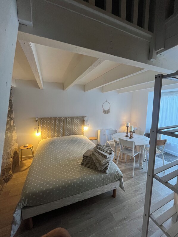 A bedroom with a bed, a desk, and a chair. There is a ladder in the corner.