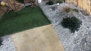Een terras met een klein gazon, zitplaatsen en decoratieve planten.