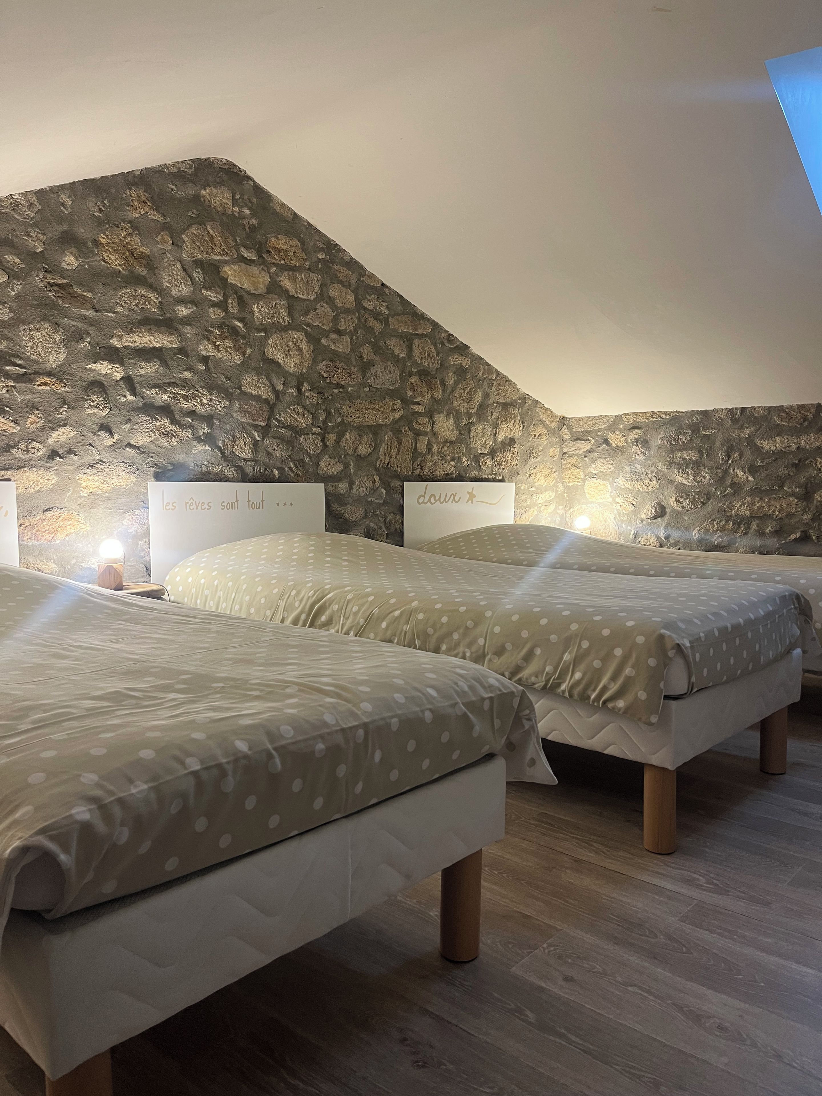 A bedroom with two beds, a stone wall, and a sloped ceiling.