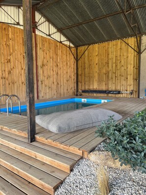 A covered outdoor swimming pool with wooden decking and a bench.