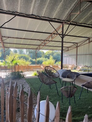 Un patio techado al aire libre con techo de metal, piscina y mobiliario exterior.