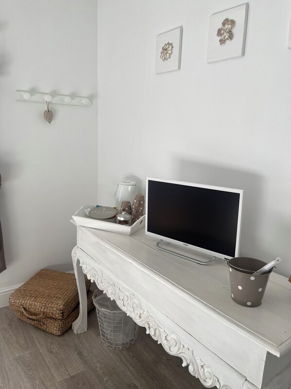 Un mueble blanco para televisor con un televisor de pantalla plana, una tetera y una olla con lunares.