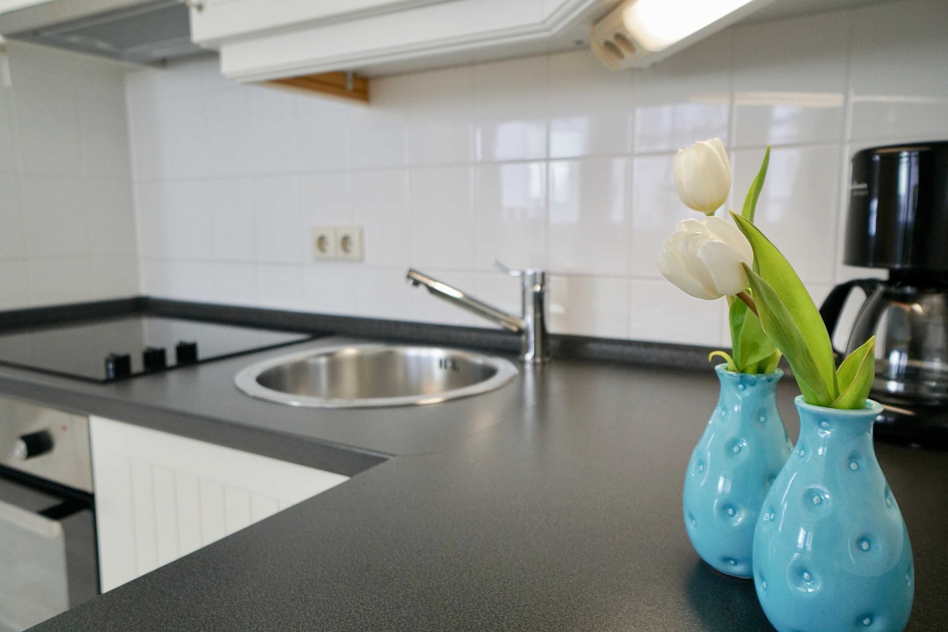Eine Küche mit schwarzem Arbeitsplatz, einer Edelstahlspüle und zwei blauen Vasen mit weißen Tulpen.