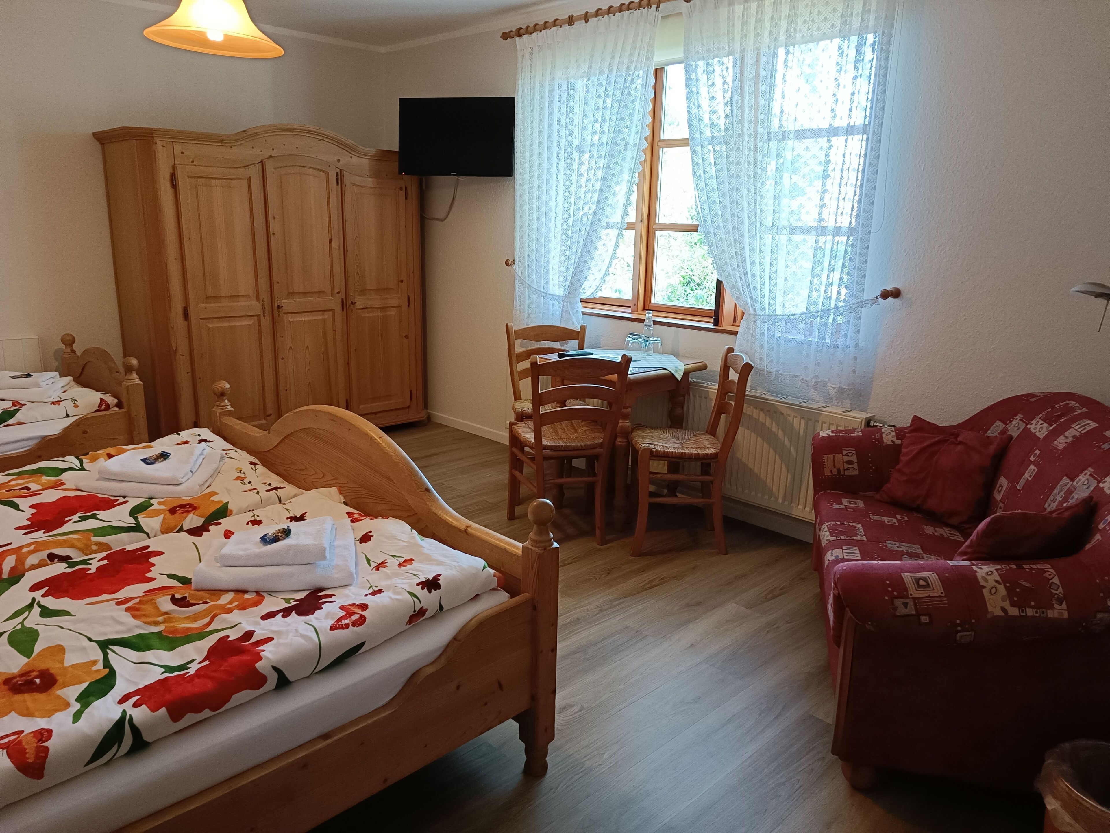 A bedroom with a wooden bed, a desk with a chair, a red sofa, and a wardrobe.