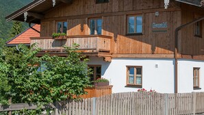 Een houten chalet met balkon, een bord met de tekst 'Gewald' en een berg op de achtergrond.