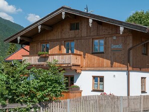 Un chalet en bois doté d’un balcon, une enseigne indiquant « Gewald », et une vue sur les montagnes en arrière-plan.