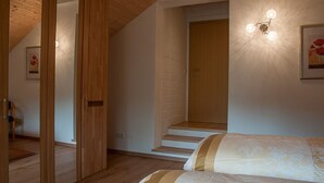 Een slaapkamer met een houten plafond, een bed met beddengoed met een patroon, een trap en een lamp aan de muur.