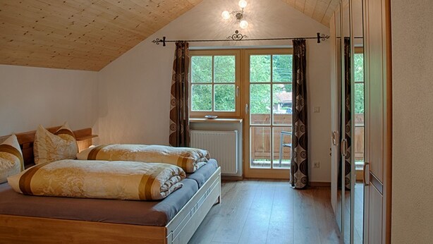 Een slaapkamer met een houten plafond, een bed met beddengoed met een patroon, een radiator en een raam met gordijnen.