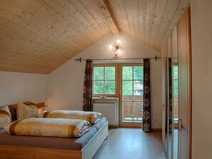 Un dormitorio con techo de madera, una cama con ropa de cama estampada, un radiador y una ventana con cortinas.