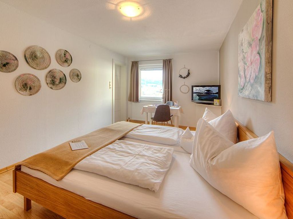 Ein Hotelzimmer mit einem hölzernen Bett, einem Schreibtisch, einem Stuhl, einem Fernseher und Wandbildern.