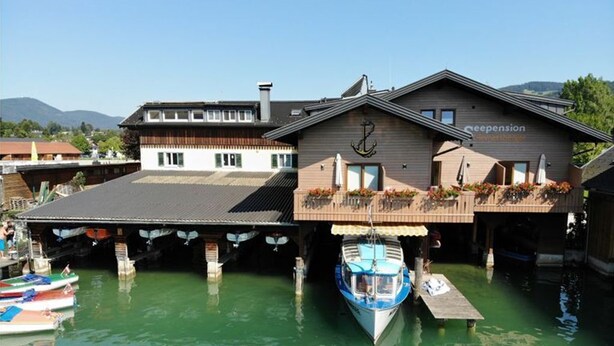 Un edificio frente al agua con un muelle, un barco y montañas al fondo.