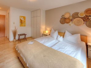 A neatly arranged bedroom with a large bed, a bedside table with a lamp, a wardrobe, and a wall decorated with woven baskets. - Double room Wartenfels - Seepension Hemetsberger (Mondsee)