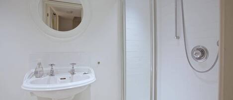 A bathroom with a white pedestal sink, a round mirror, and a glass-enclosed shower.