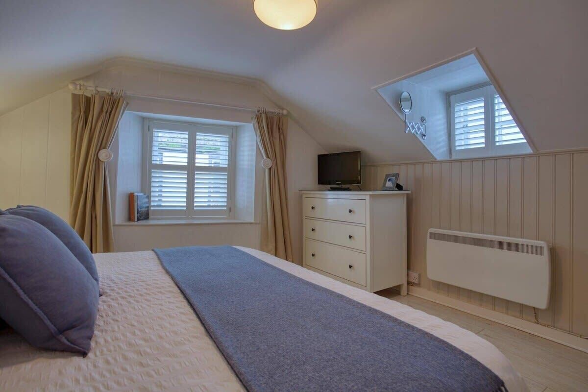 A bedroom with a bed, a dresser, a television, and a skylight.