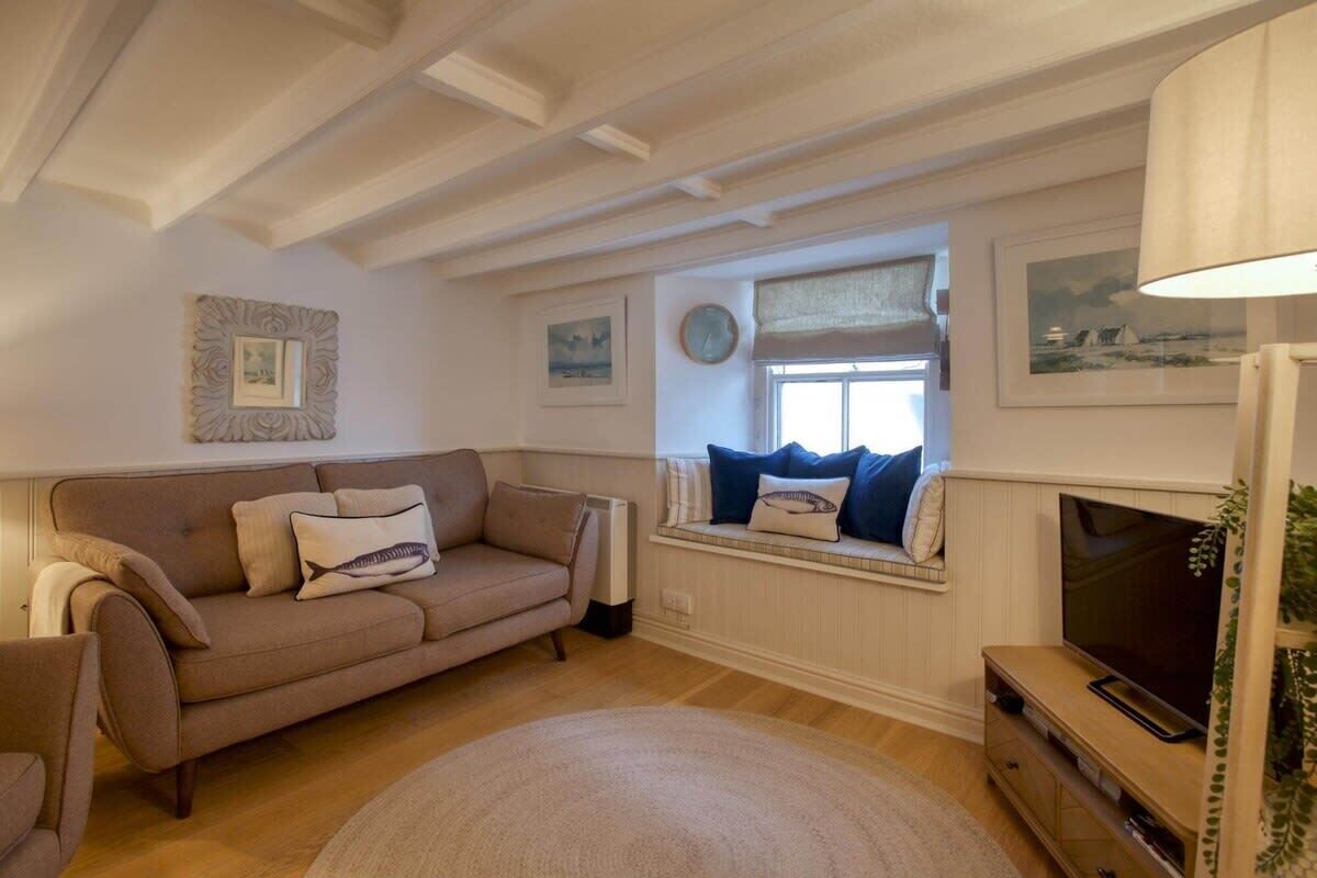 A living room with a beige sofa, a television on a wooden stand, and a window with a view of the outside.