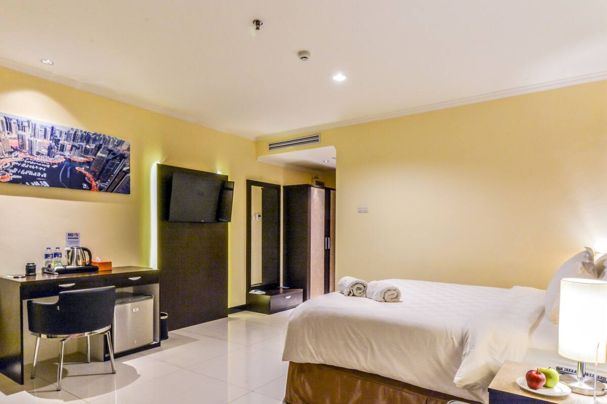 A hotel room with a bed, a desk with a chair, a television, and a bathroom.